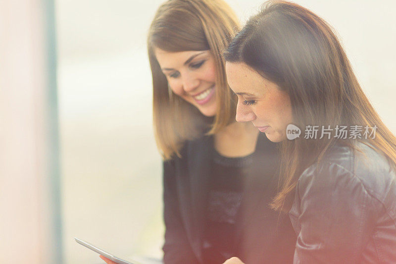 Two friends using digital tablet on bus station